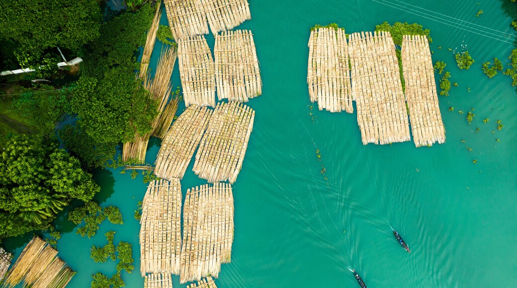 Vue aérienne d’un système de radeaux flottants en bambou sur une étendue d’eau turquoise, entourée d’une végétation luxuriante.