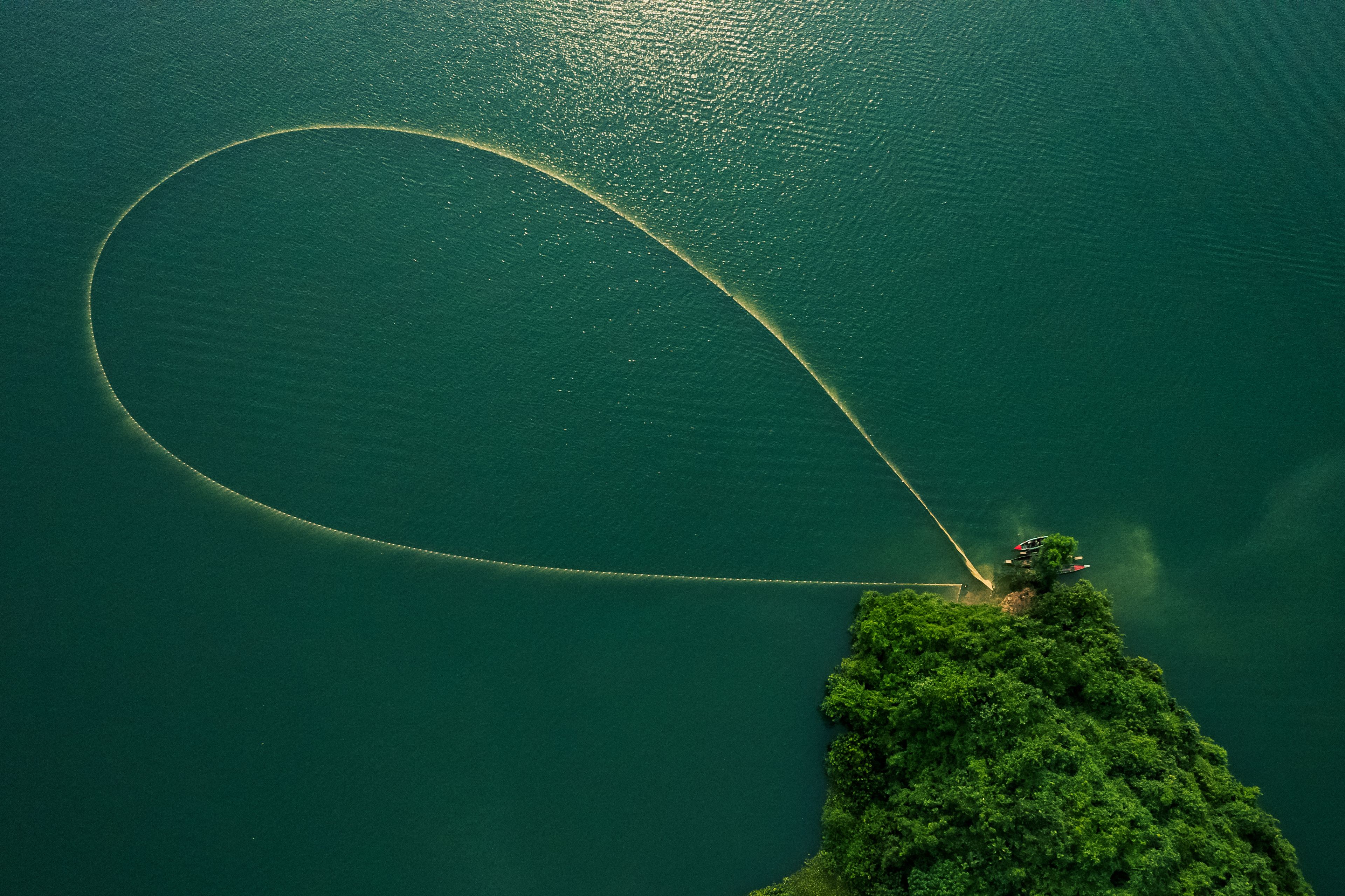 Une vue aérienne d’un lac où un bateau laisse derrière lui une large traînée.