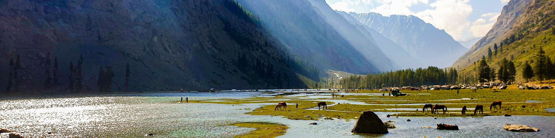 A mountainous landscape with a river, horses grazing, and a village in the valley.