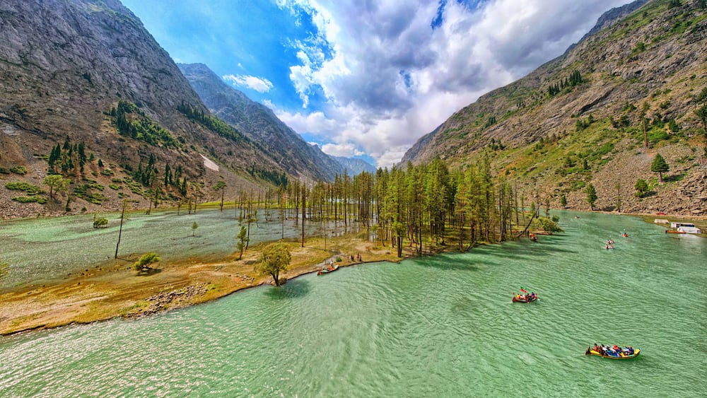 A river surrounded by mountains, clear water, and a few boats.