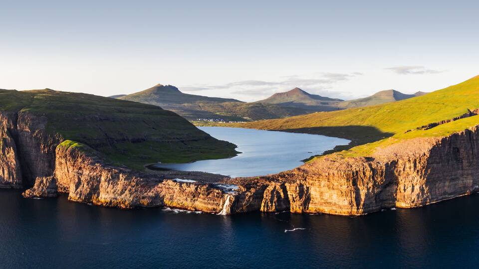 A rugged coastline with steep cliffs, a calm bay, and distant mountains.