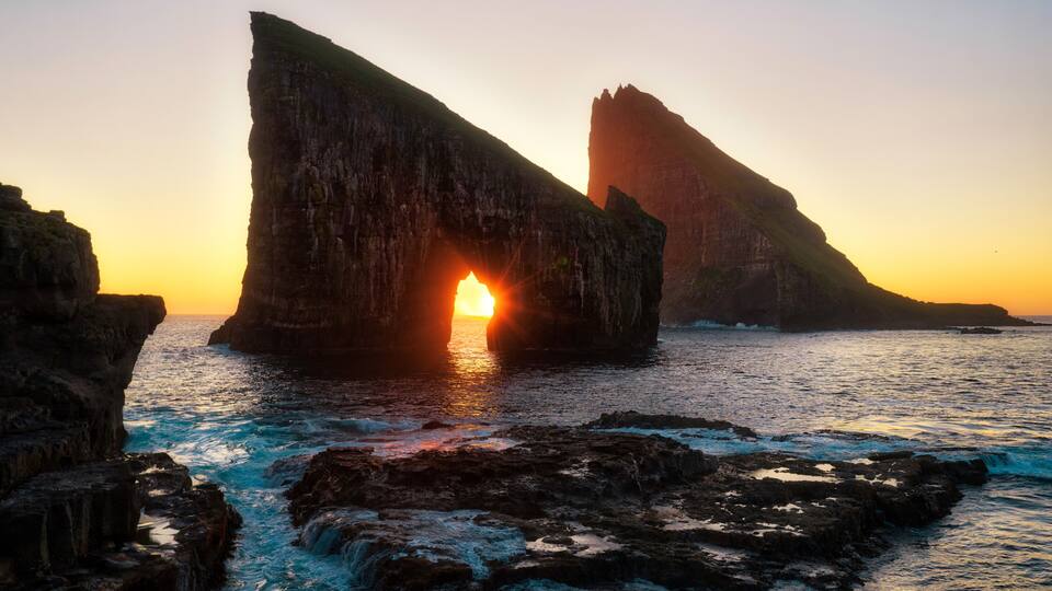 A sunset over a coastal rock formation with waves crashing against the rocks.