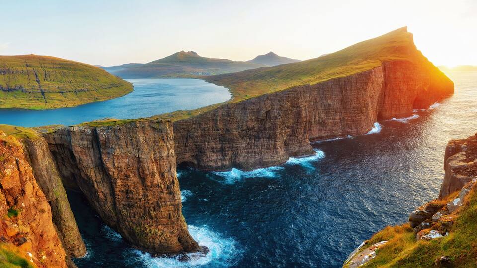 A coastal landscape with cliffs, a body of water, and distant hills.