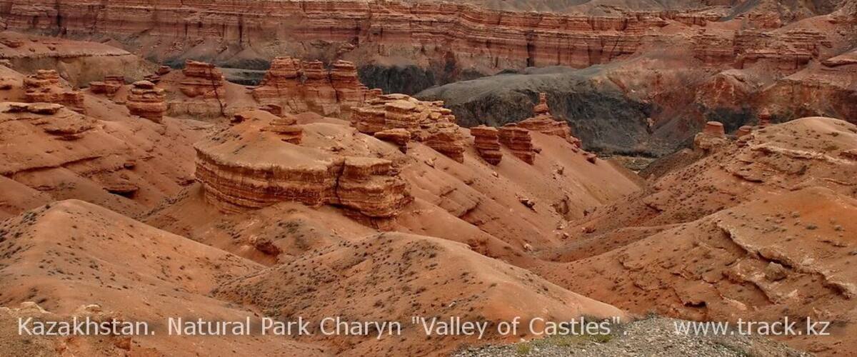A rugged landscape with layered rock formations and a distant snow-capped mountain range.