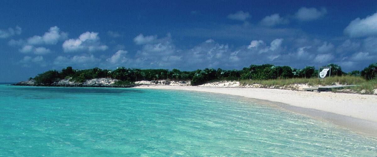 Clear turquoise water, a sandy beach, and a distant shoreline with greenery.