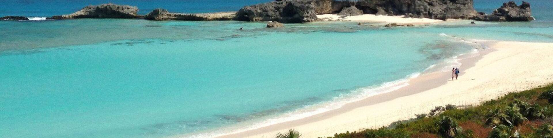 A beach with clear turquoise waters, white sand, and rocky formations.