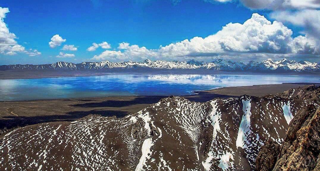 Un paisaje montañoso con picos nevados, una masa de agua extensa y un cielo azul despejado.