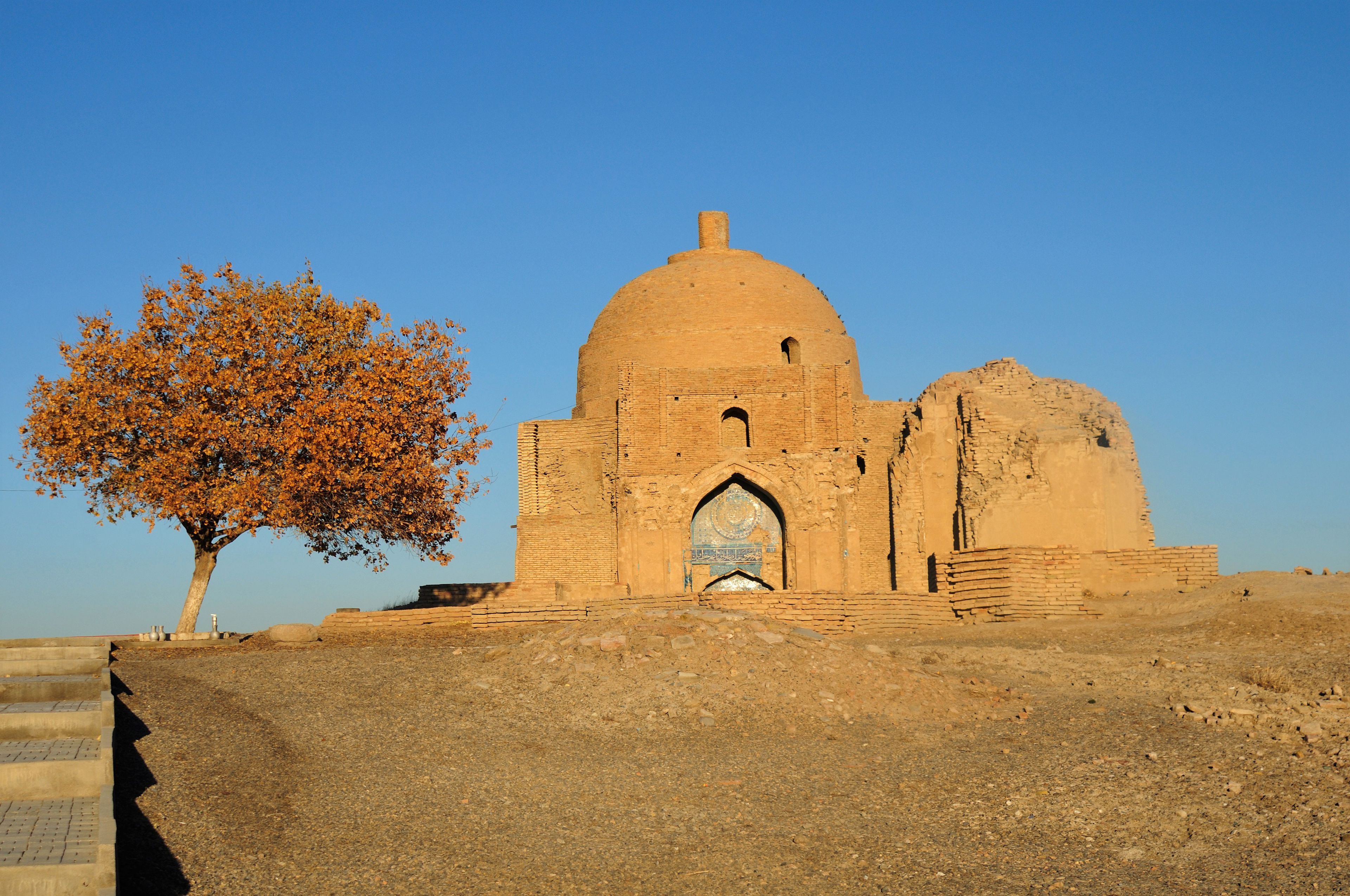 A historical building with a dome and arched entrance, surrounded by a dry landscape.