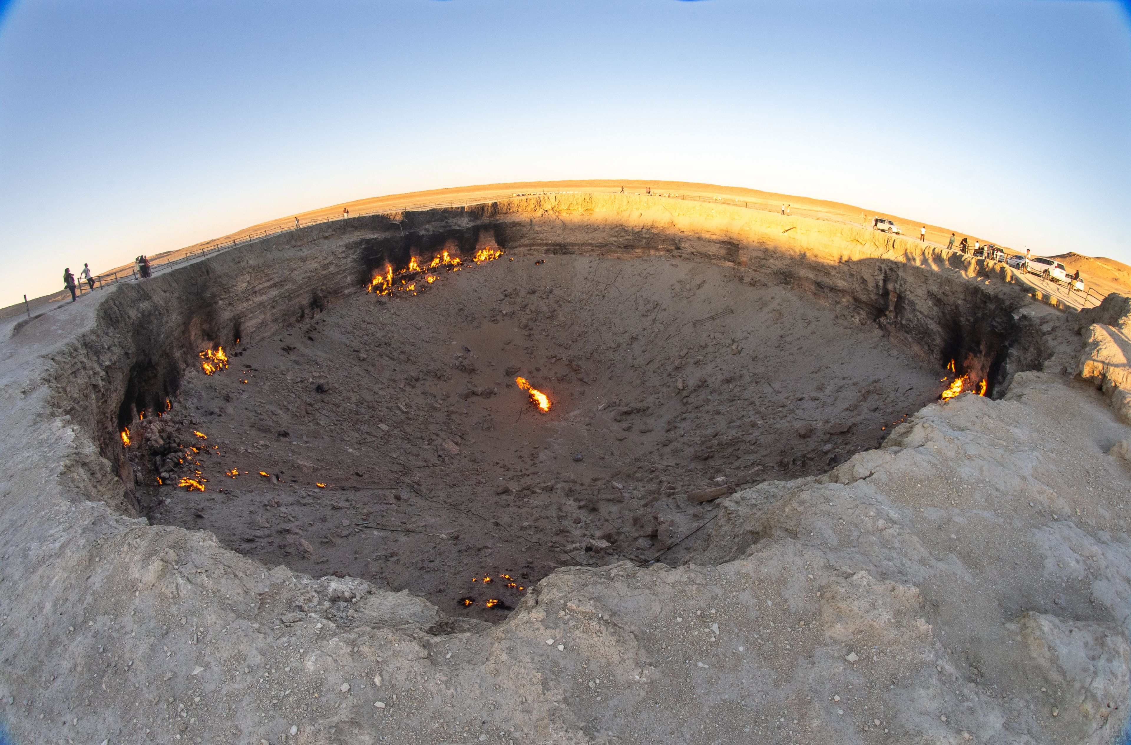 A large, circular excavation site with visible fire pits and a fenced perimeter.