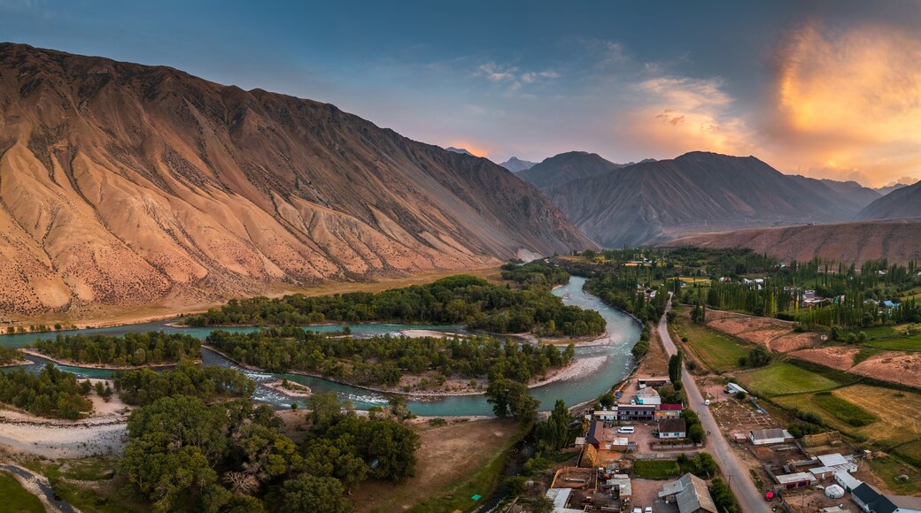 Aerial view of the Kyzyl-Oi village nestled in a lush river valley surrounded by dramatic arid mountains under a golden sunset sky in Kyzyl-Oi, Chuy Province, Kyrgyzstan.