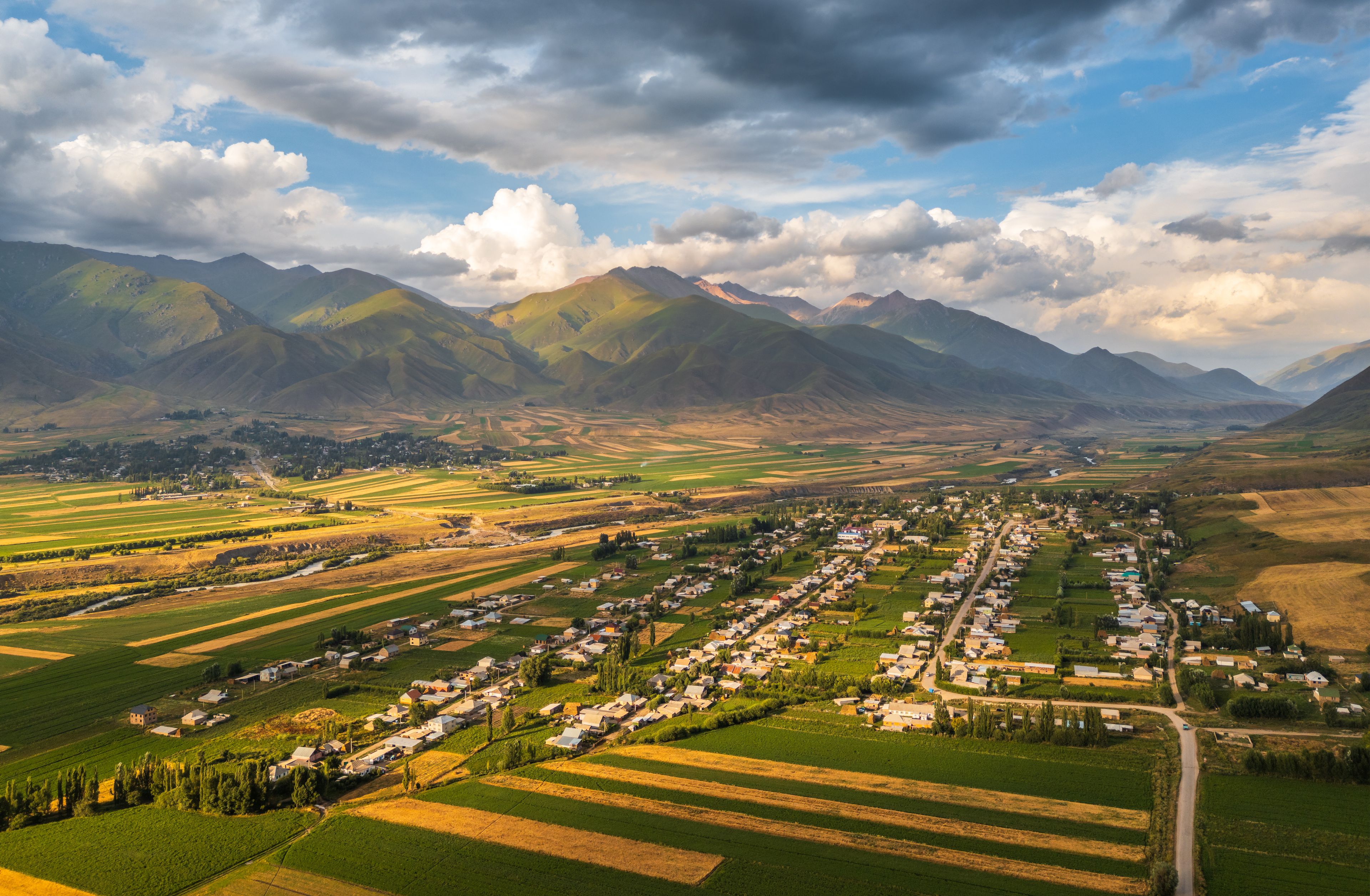 Aerial view of Chon-Kemin valley featuring the village of Kemin nestled among lush agricultural fields and rolling mountains under a dramatic cloudy sky in Kemin, Chuy Province, Kyrgyzstan.