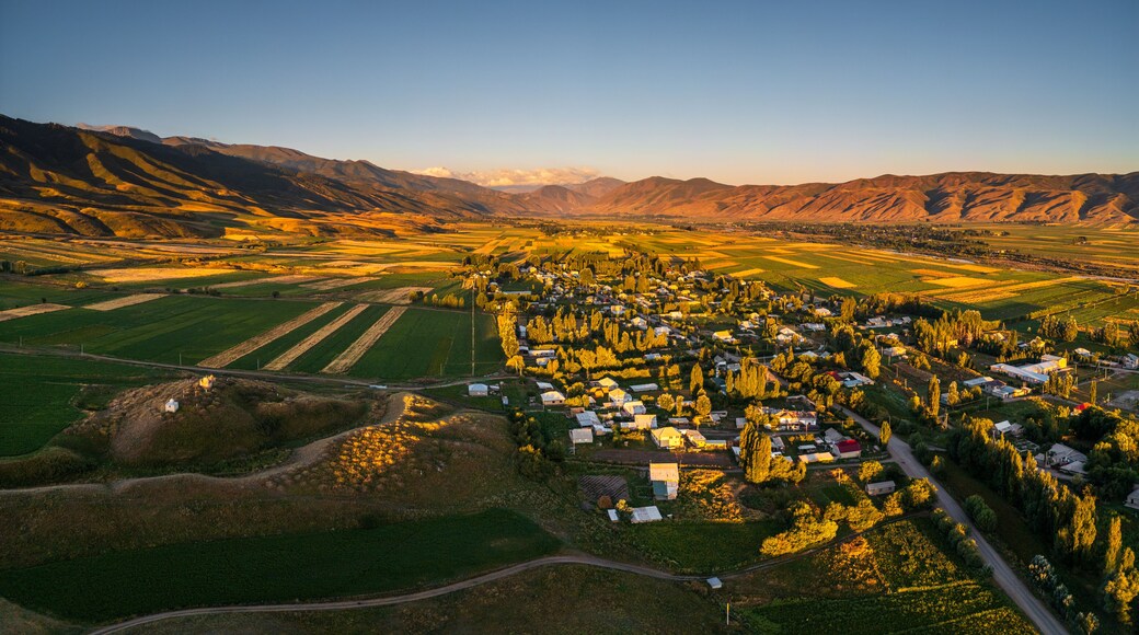 Aerial view of the Chon-Kemin valley village with agricultural fields and rolling mountains under the golden light of sunset in Kaindy, Chuy Province, Kyrgyzstan.