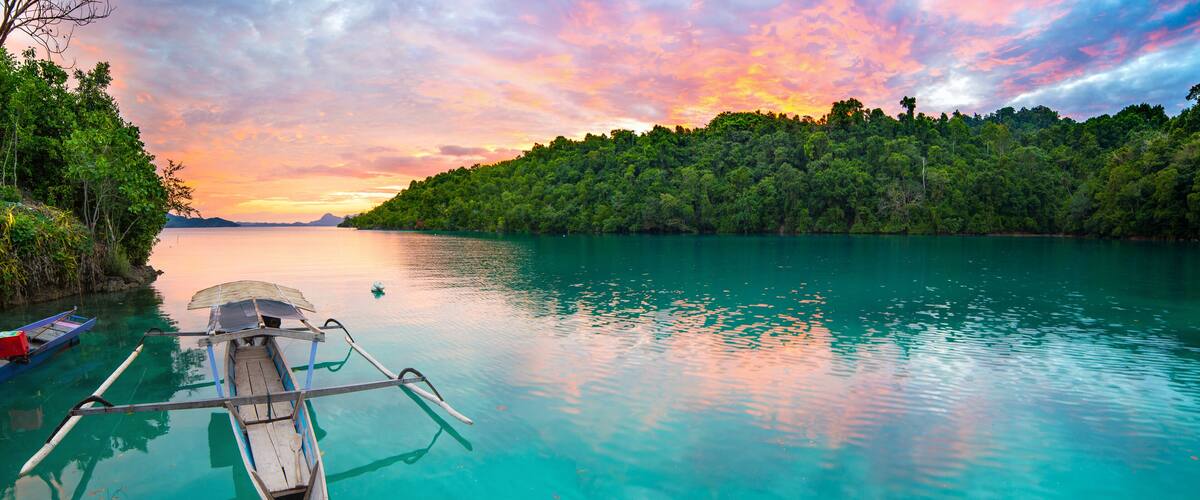 Breathtaking colorful sunset and traditional boat floating on scenic blue lagoon in the Togean (or Togian) Islands, Central Sulawesi, Indonesia, upgrowing travel destination.