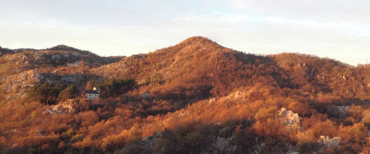 A mountainous landscape with autumn foliage and a small building on a hill.