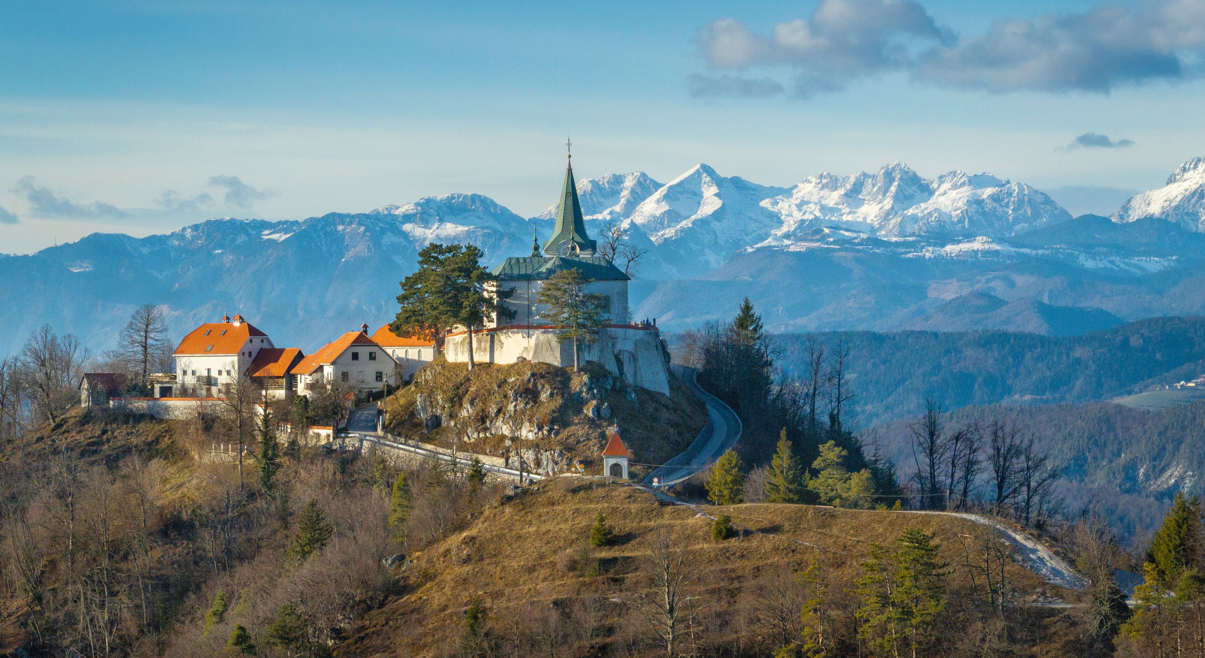 A castle on a hill with snow-capped mountains in the background.