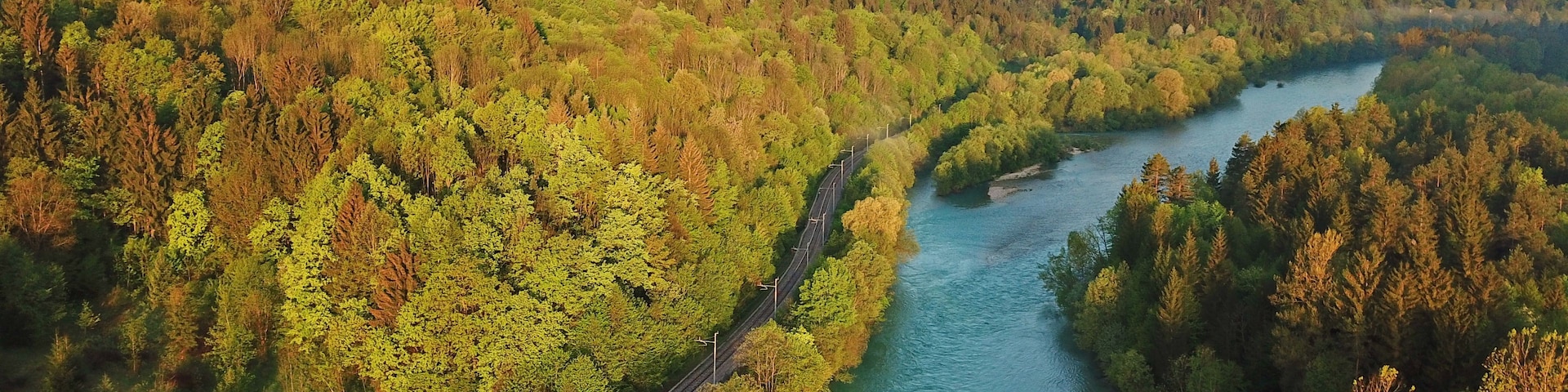 Un río serpentea por un valle boscoso con una vía de tren a su lado.