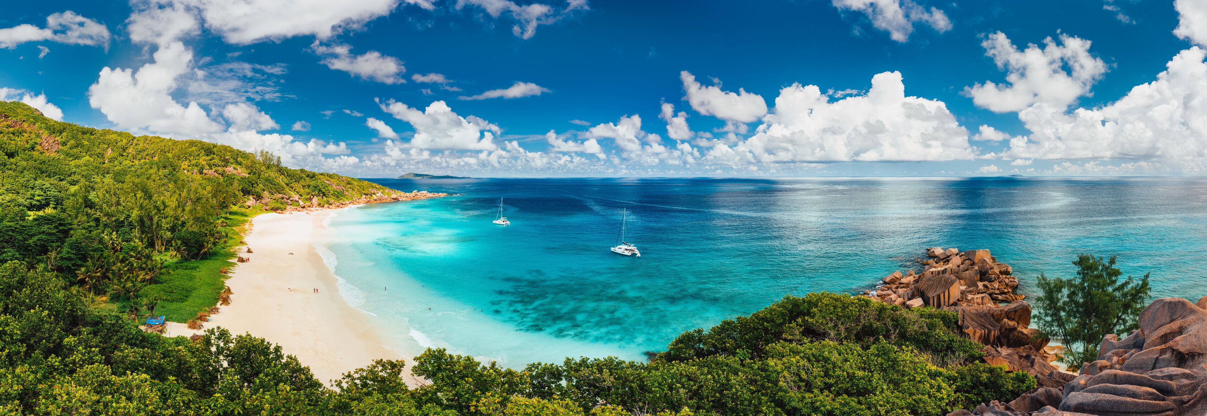 Aerial Pano of Grand Anse beach at La Digue island in Seychelles. White sandy beach with blue ocean lagoon and catamaran yacht moored