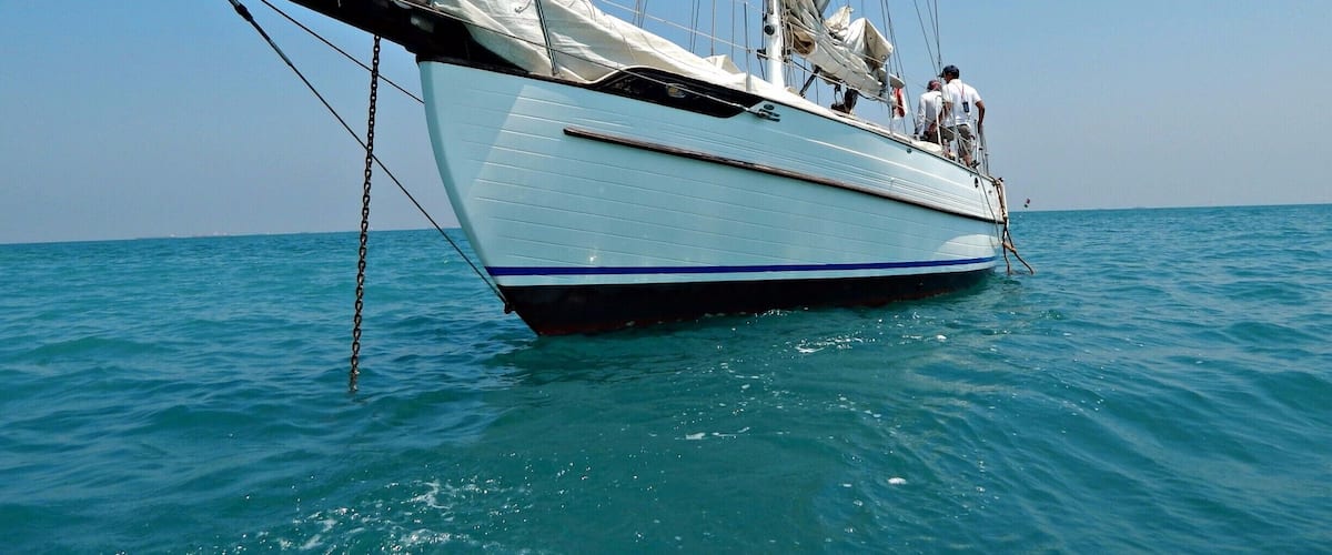 A sailboat with a white hull and blue stripe, anchored in calm blue waters under a clear sky.