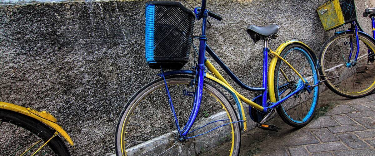 A blue and yellow bicycle with a basket, parked on a cobblestone street.
