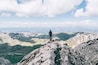 Una persona in piedi sulla cima di una montagna rocciosa, con vista panoramica su montagne innevate e valli.