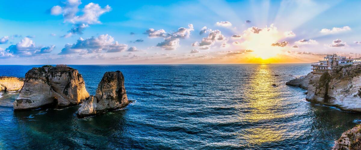 Brown rock formation on sea under blue sky and white clouds