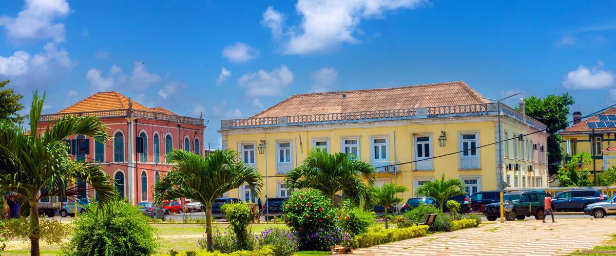 A street with colorful buildings, palm trees, and parked cars.