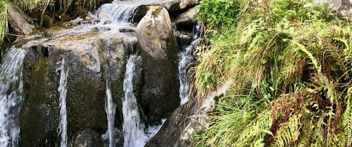 A small waterfall in a lush, green valley with rocky terrain and dense vegetation.