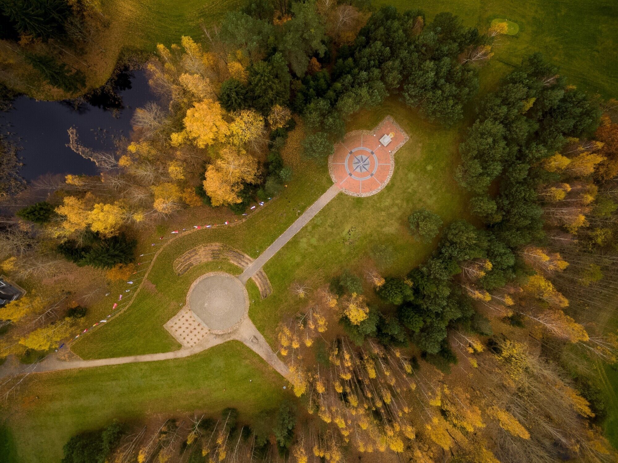 En vy över en park från ovan, med ett runt monument, en damm och träd runt omkring.