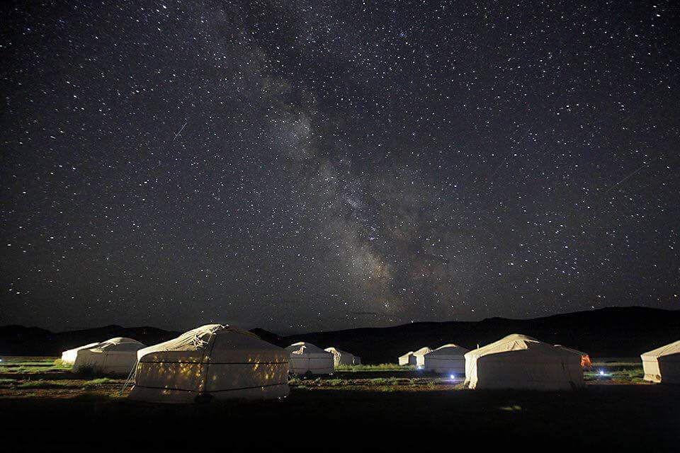 Cielo estrellado sobre yurtas en un entorno rural.