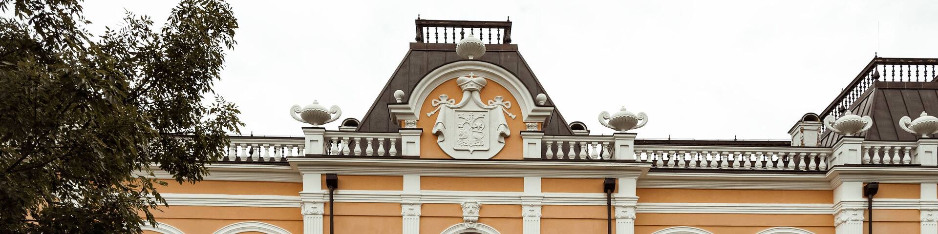 A historic building with ornate architecture, a large central door, and a reflection in the water in front.