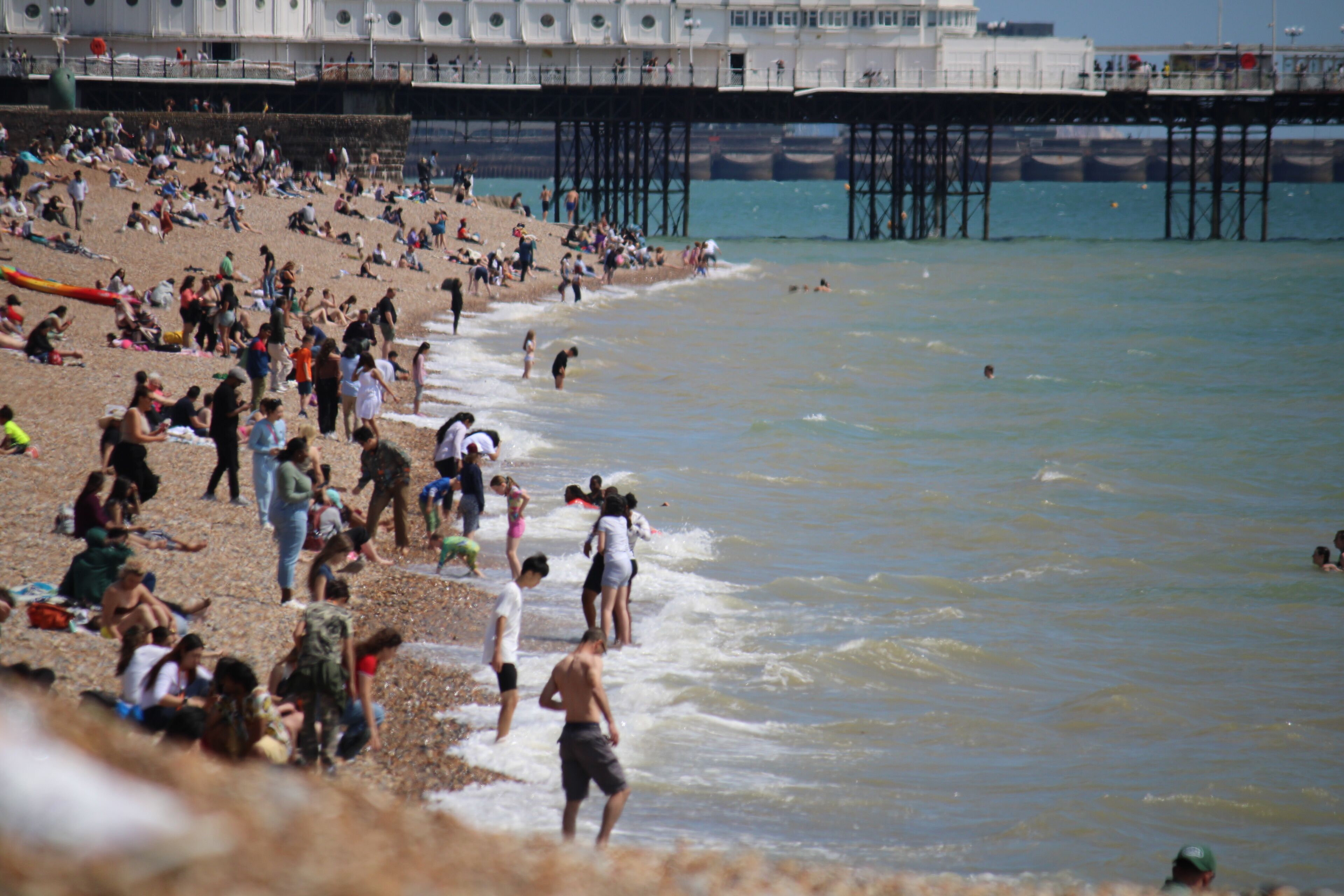 Brighton beach, East Sussex, UK - 08.08.2024: Brighton beach people sunbathing on shingle pebble beach sunny day with blue sky, Brighton pier behind