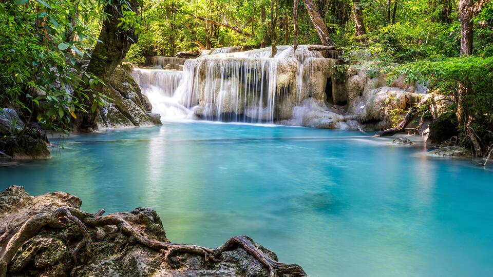 A waterfall cascading into a clear blue pool surrounded by lush greenery.