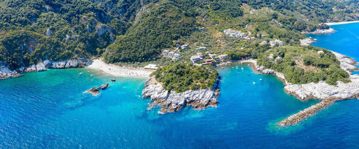 An aerial view of a coastal area with clear turquoise waters, rocky outcrops, and a small beach.