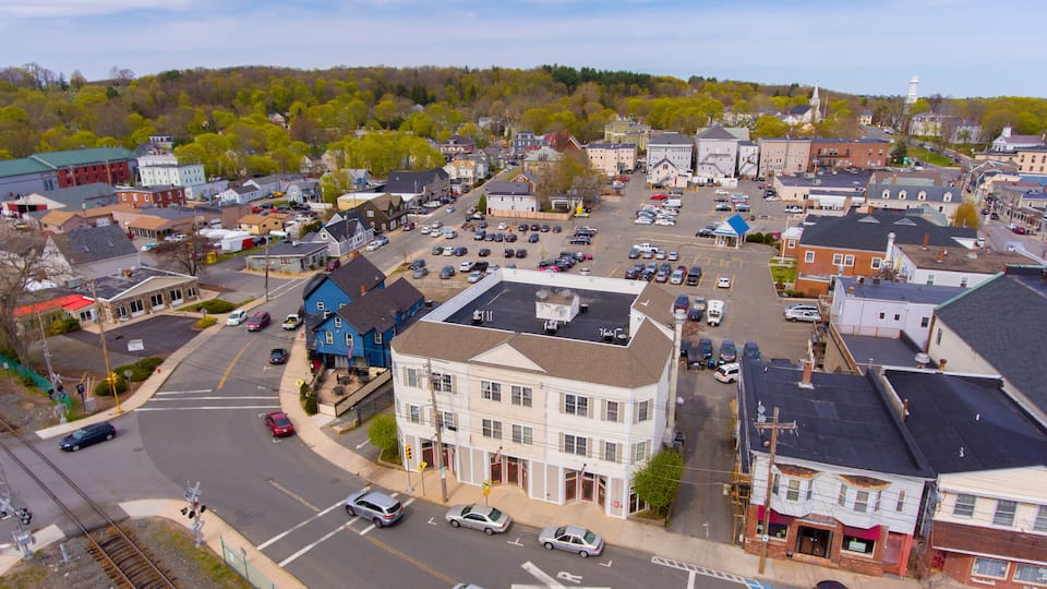 An aerial view of a small town with a mix of residential and commercial buildings, a railway crossing, and a parking lot.