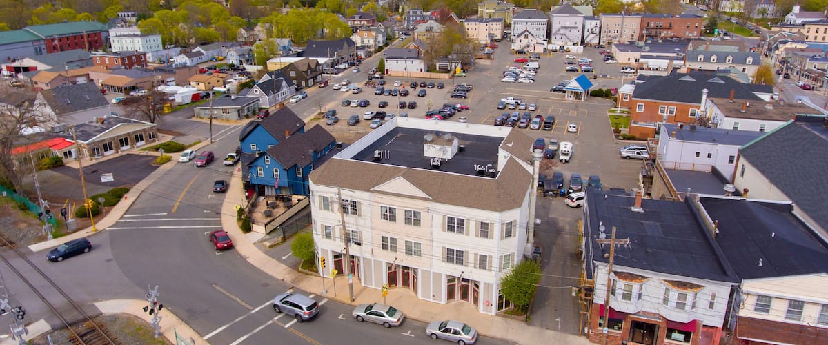 An aerial view of a small town with a mix of residential and commercial buildings, a railway crossing, and a parking lot.