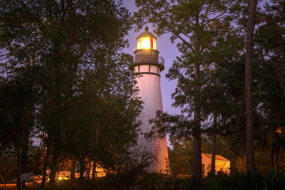 A lighthouse surrounded by trees at dusk.