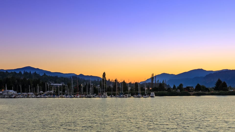 A marina with boats docked at sunset with mountains in the background.