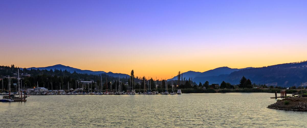A marina with boats docked at sunset with mountains in the background.