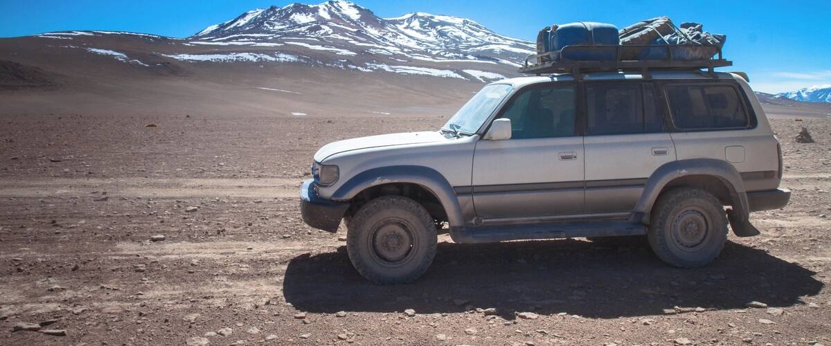 A white SUV parked on a rocky terrain with a snow-capped mountain in the background.