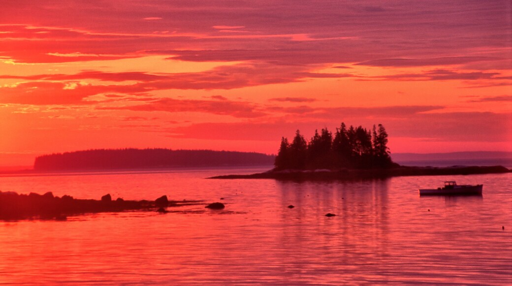 Vibrant red sky with sun about to rise over the horizon. Tranquil coastal scene near South Thomaston, Maine, with distant islands and lobster boat anchored in calm ocean.