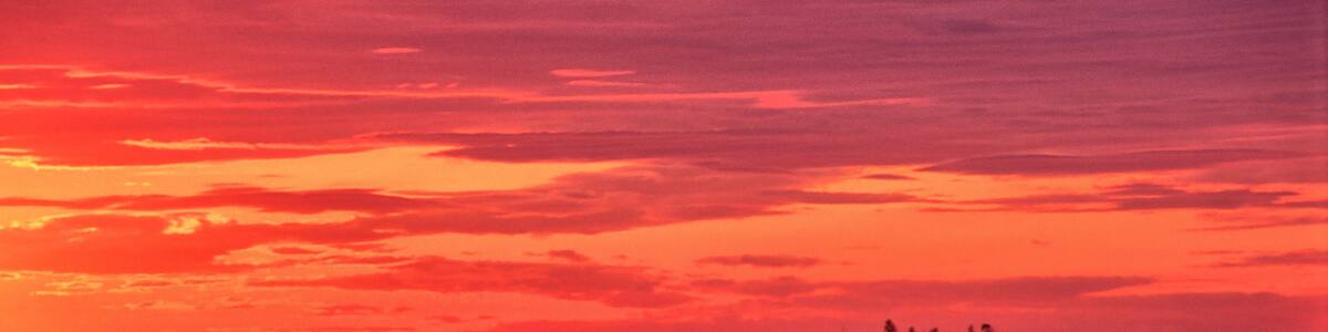 Vibrant red sky with sun about to rise over the horizon. Tranquil coastal scene near South Thomaston, Maine, with distant islands and lobster boat anchored in calm ocean.