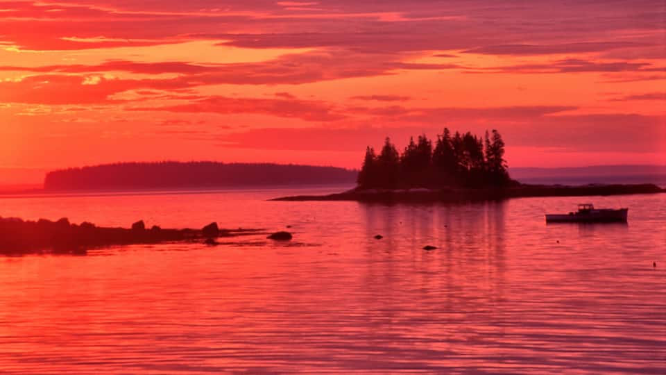 A sunset over a body of water with an island and a boat.