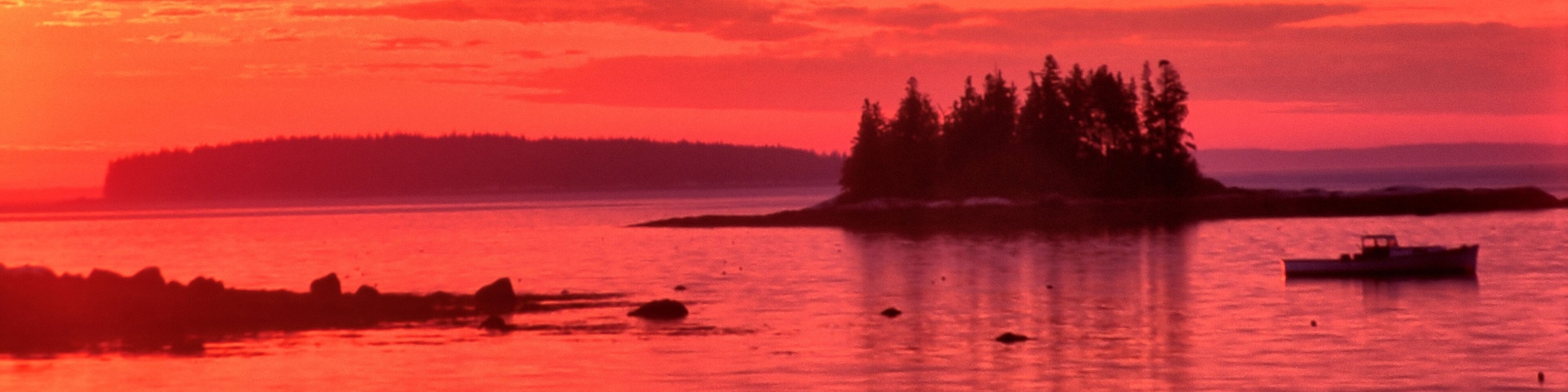Vibrant red sky with sun about to rise over the horizon. Tranquil coastal scene near South Thomaston, Maine, with distant islands and lobster boat anchored in calm ocean.