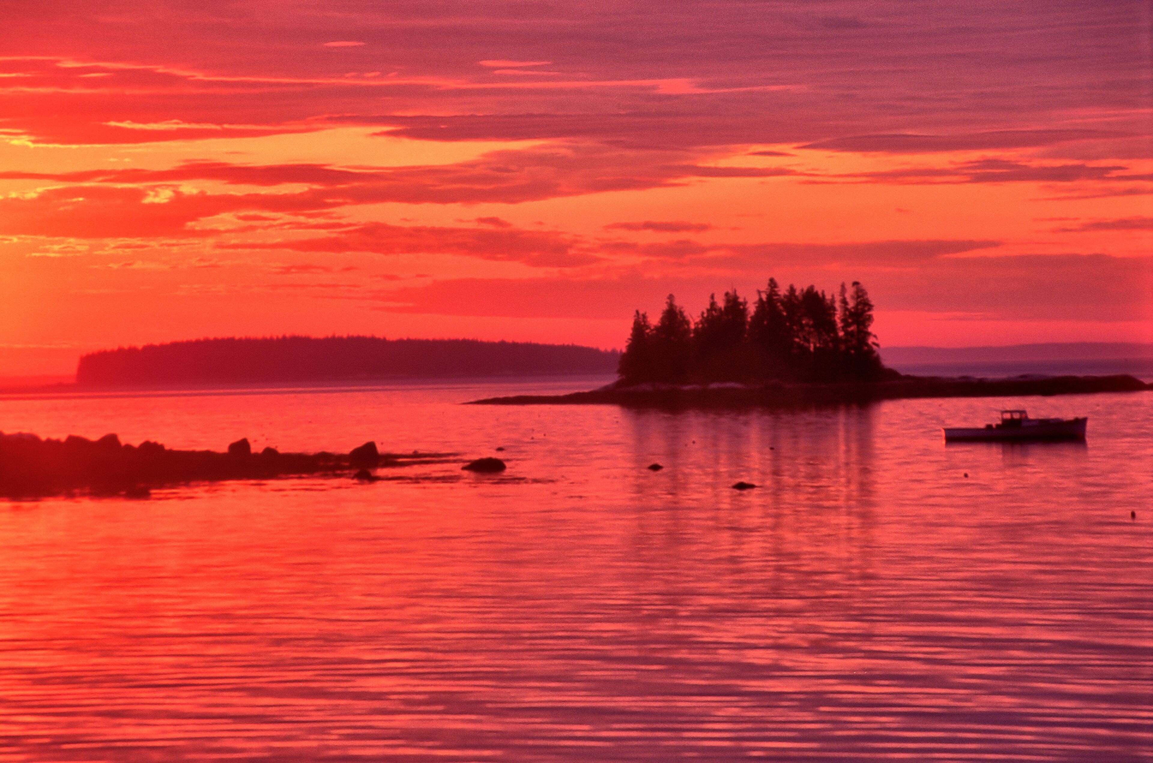 A sunset over a body of water with an island and a boat.