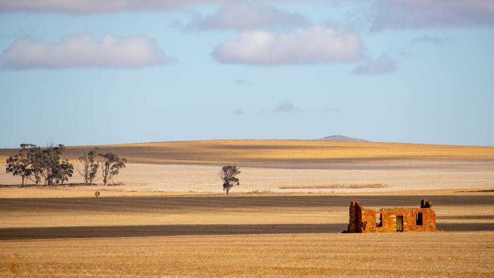 A vast, flat landscape with a small, dilapidated structure in the foreground and a distant hill.