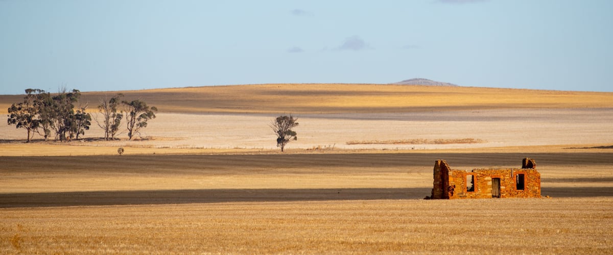 A vast, flat landscape with a small, dilapidated structure in the foreground and a distant hill.