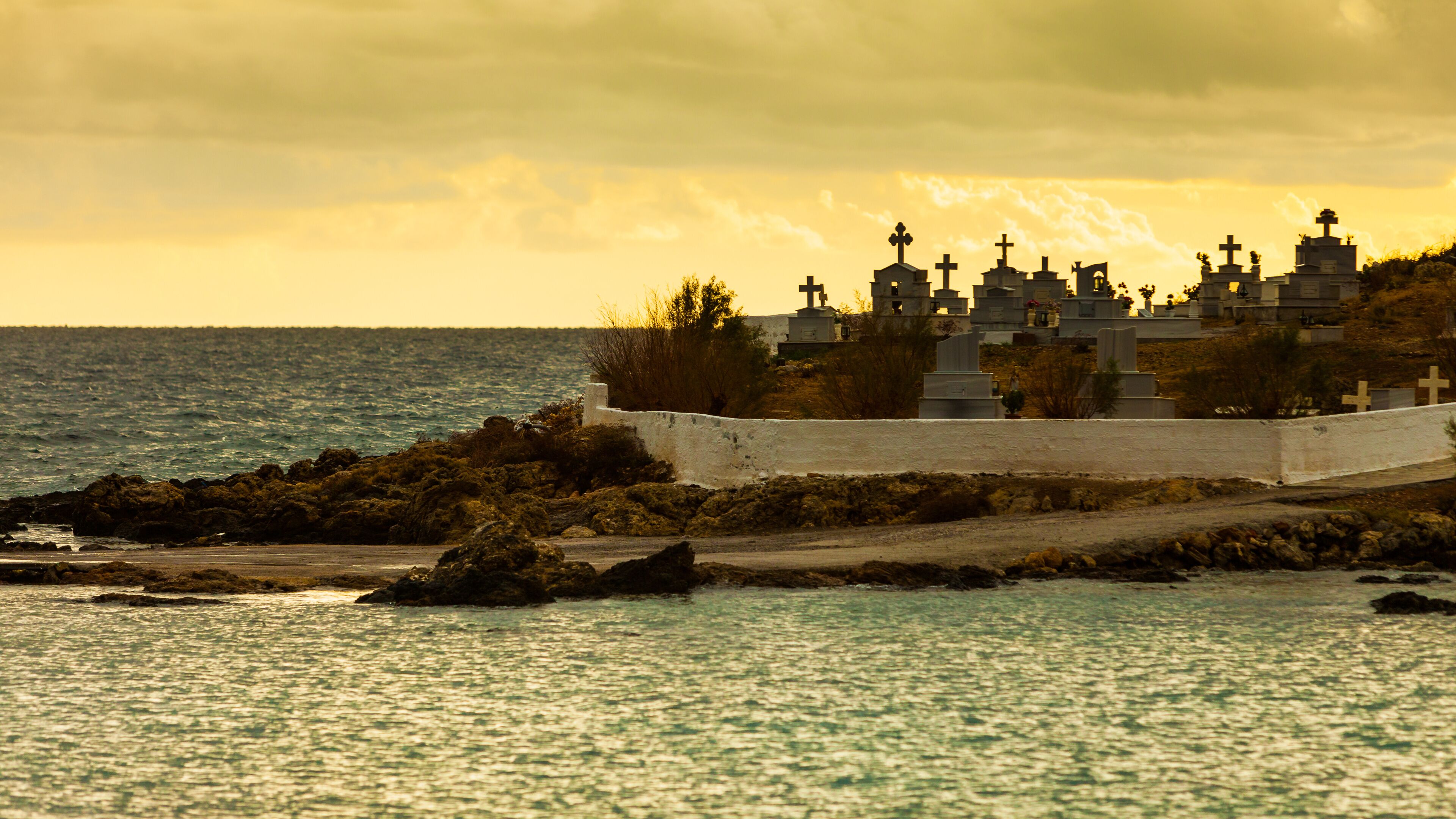 A coastal cemetery with numerous crosses and tombstones, surrounded by rocky terrain and the sea.
