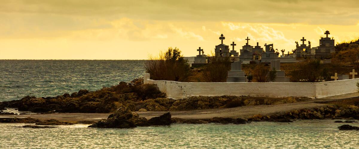 A coastal cemetery with numerous crosses and tombstones, surrounded by rocky terrain and the sea.