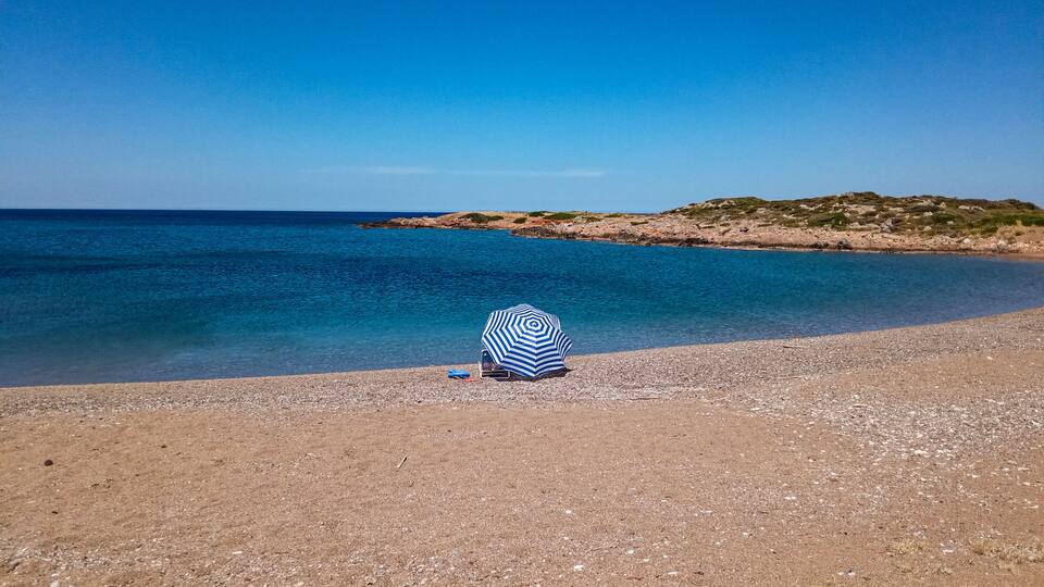 A beach with a striped umbrella and a chair on the pebbly shore.