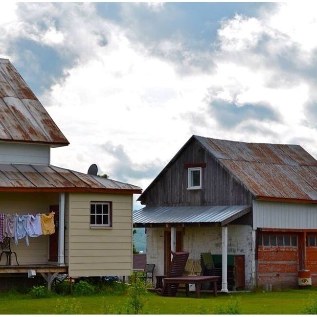 A rustic wooden house with a porch and a small shed.